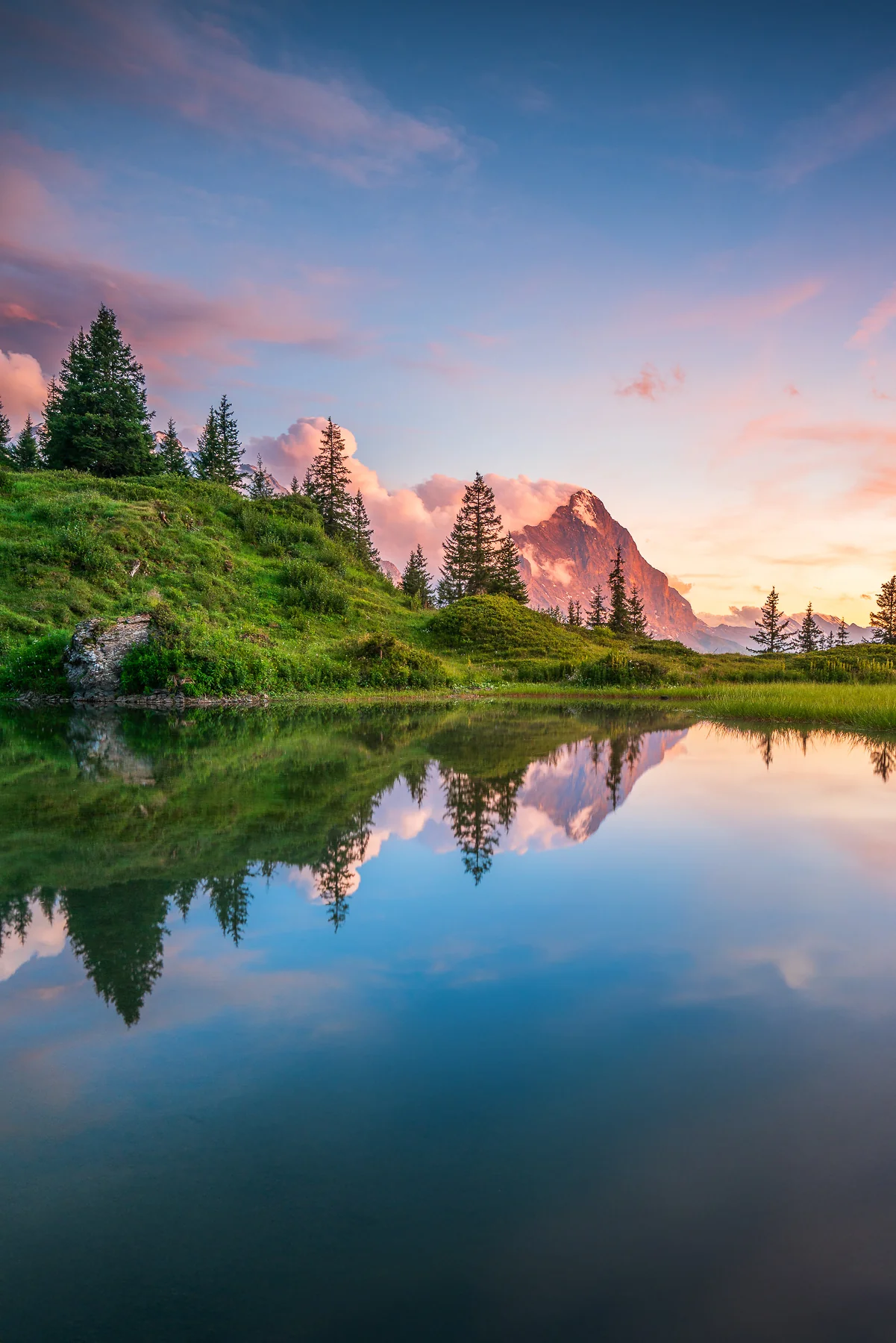 Spiegelnder Alpensee mit Tannen und Bergspitzen im Berner Oberland bei goldenem Sonnenuntergang
