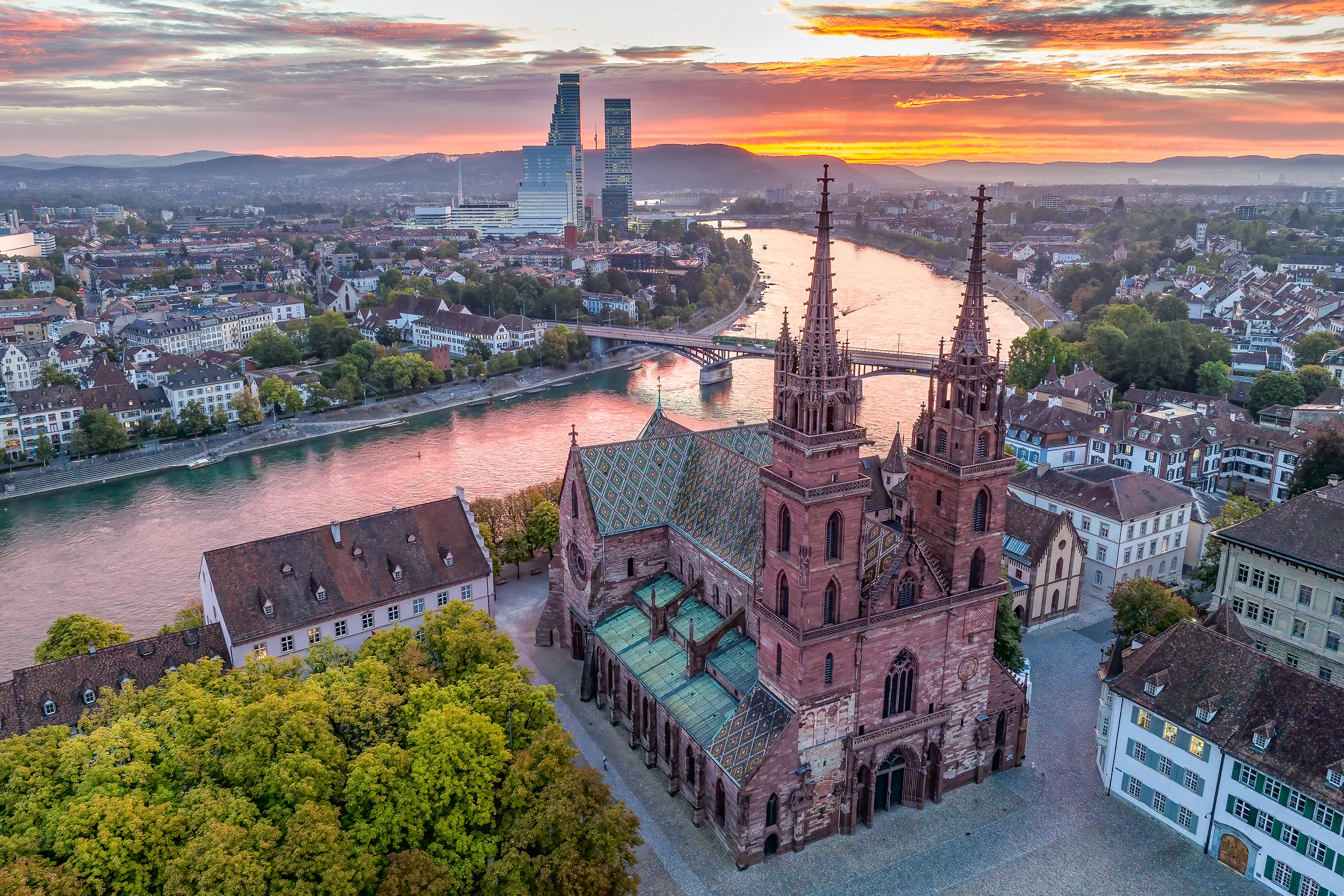 Drohnenaufnahme des Basler Münsters bei Sonnenuntergang mit Blick auf die Altstadt, den Rhein und die umliegenden Berge