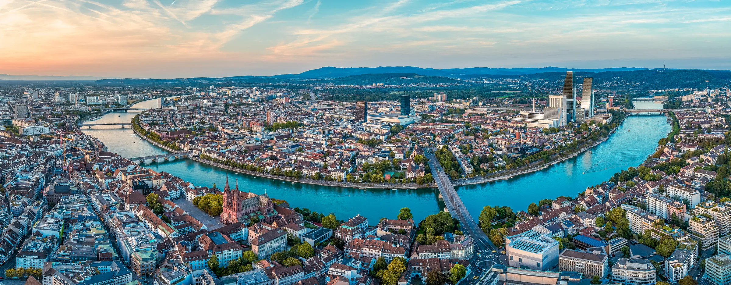 Luftaufnahme von Basels Altstadt mit dem Rhein bei Sonnenuntergang, türkisblaues Wasser und goldene Reflexionen