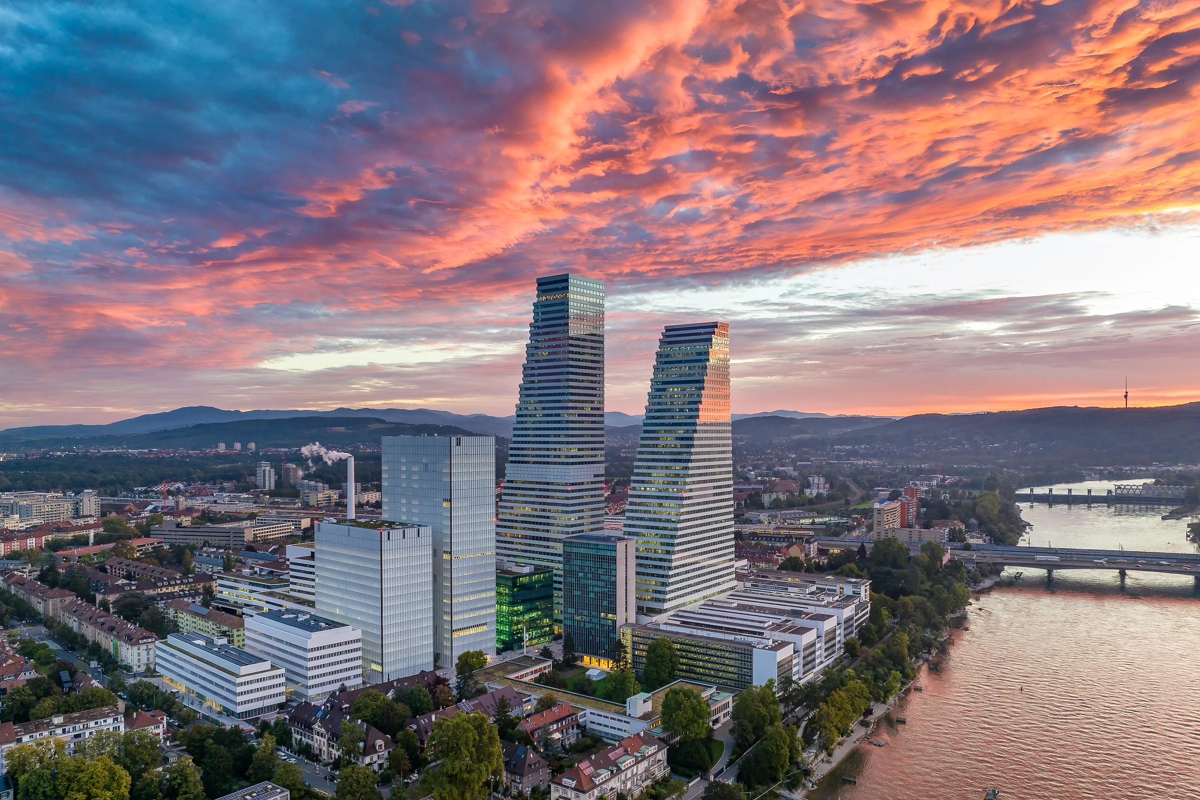Aerial-Drohnenaufnahme der Roche-Türme in Basel am Rhein mit dramatischem Sonnenuntergangshimmel