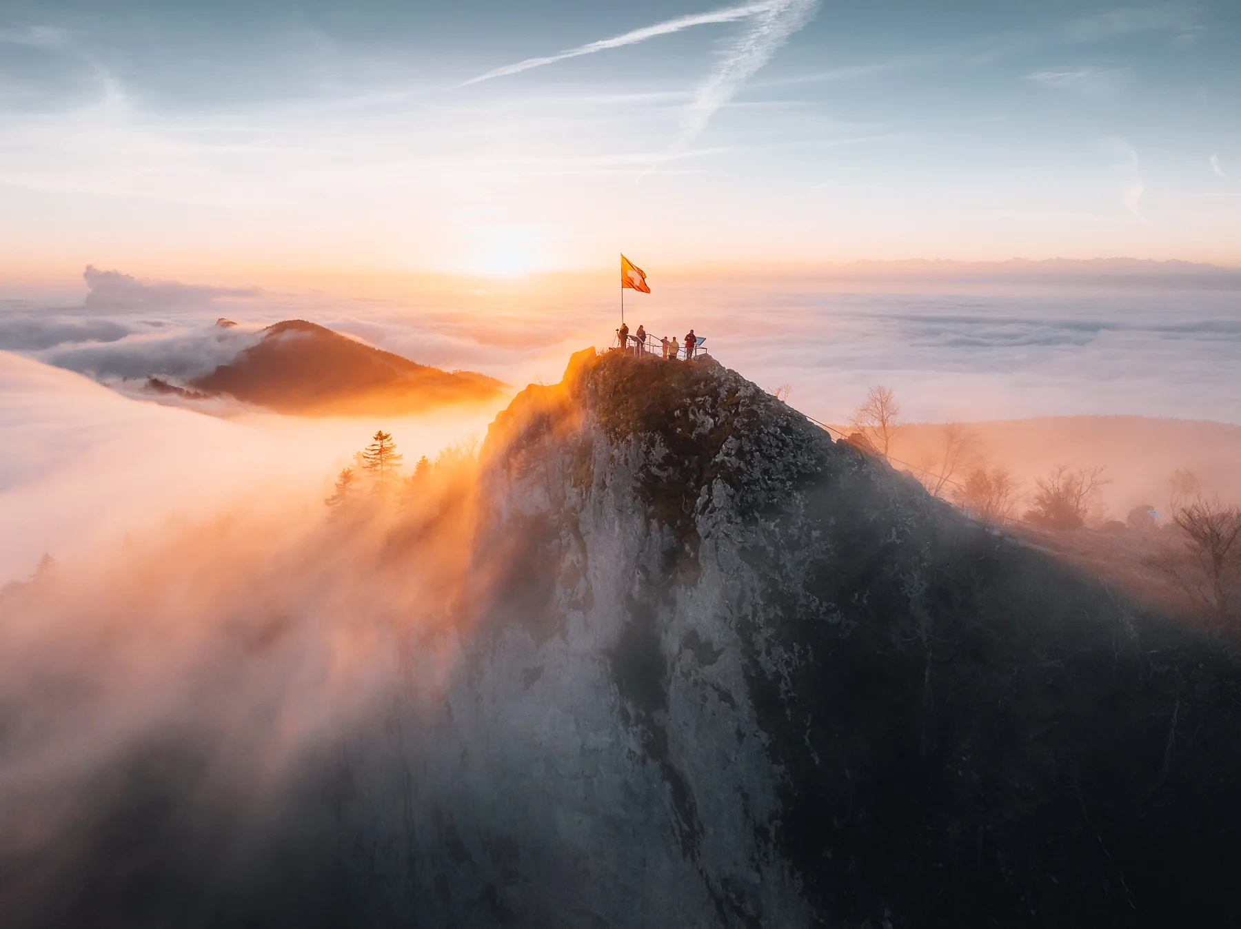 Wanderer mit Flagge auf der Belchenflue bei goldenem Sonnenaufgang über ausgedehntem Nebelmeer in den Schweizer Alpen