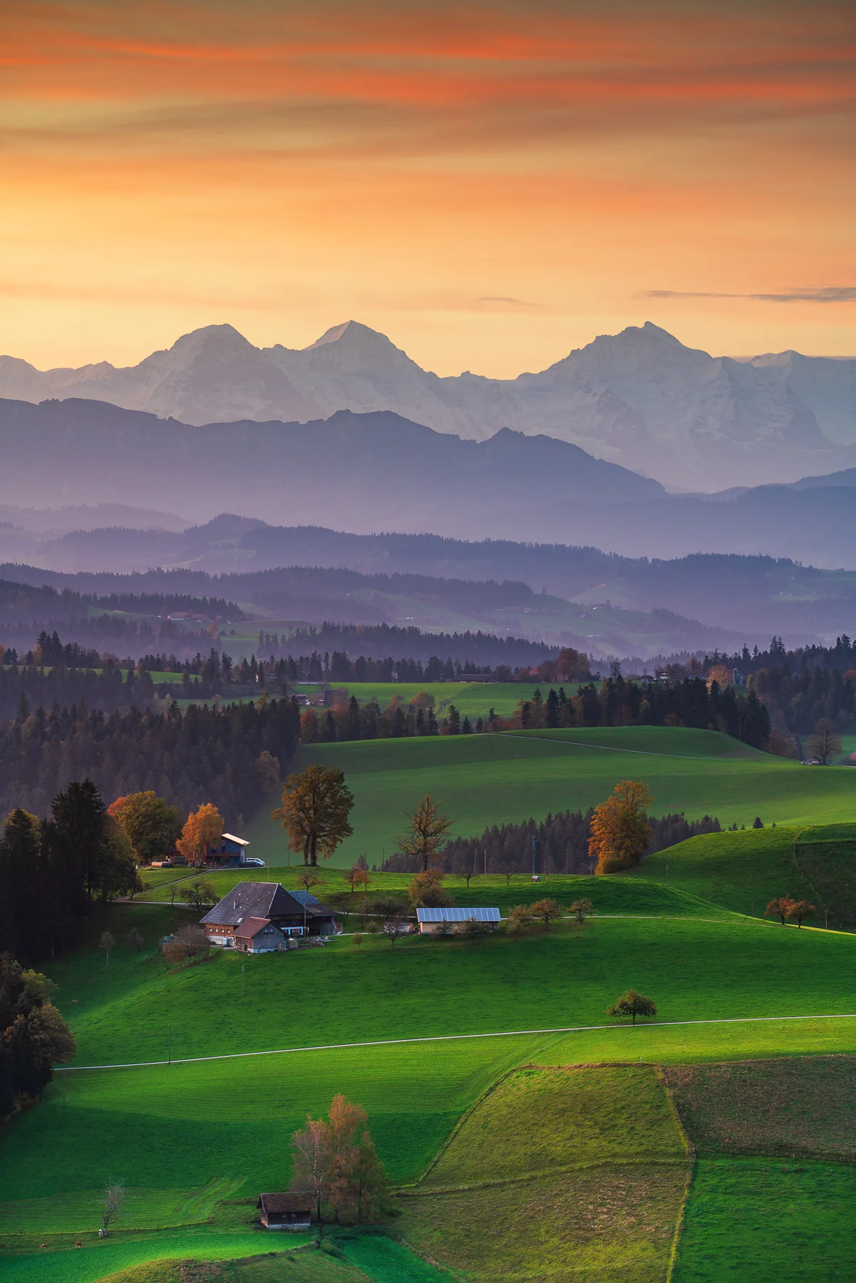 Idyllische Berglandschaft im Emmental bei Sonnenuntergang mit sanften Hügeln, grünen Wiesen, traditionellen Bauernhöfen...