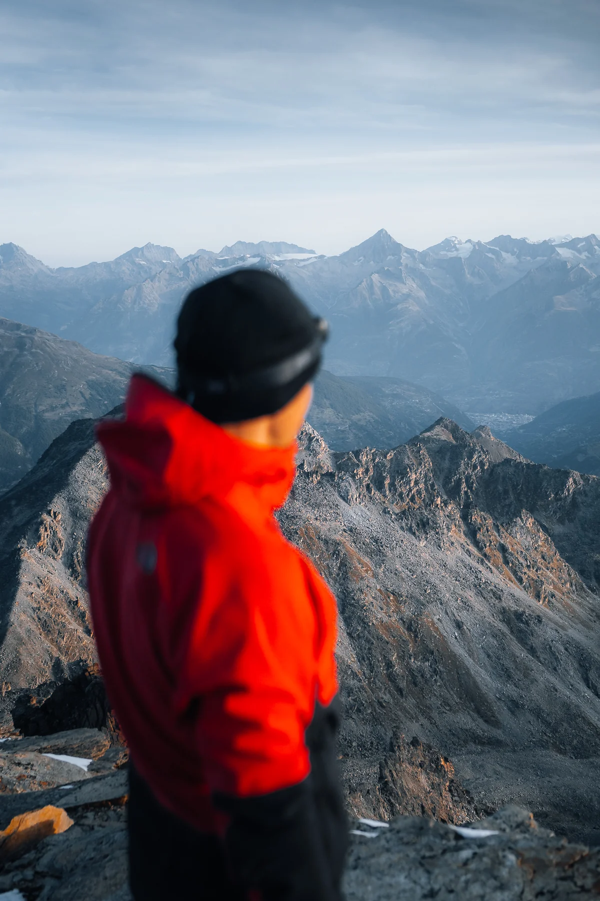 Wanderer in roter Jacke auf dem Gross Bigerhorn Gipfel mit Blick auf die Walliser Alpengipfel bei Sonnenaufgang