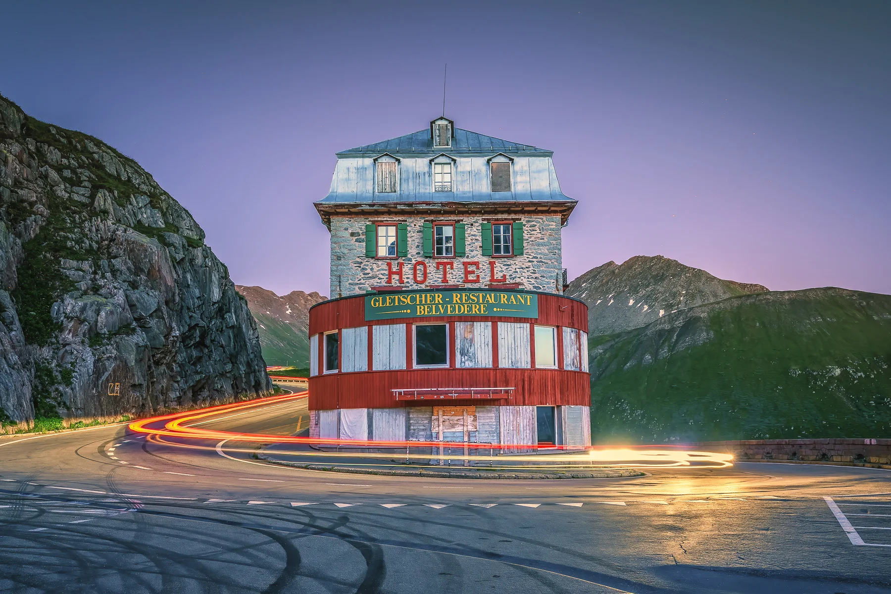 Hotel Belvedere am Furkapass bei Dämmerung mit Langzeitbelichtung, rote Lichtspur von Fahrzeugen umrundet das...
