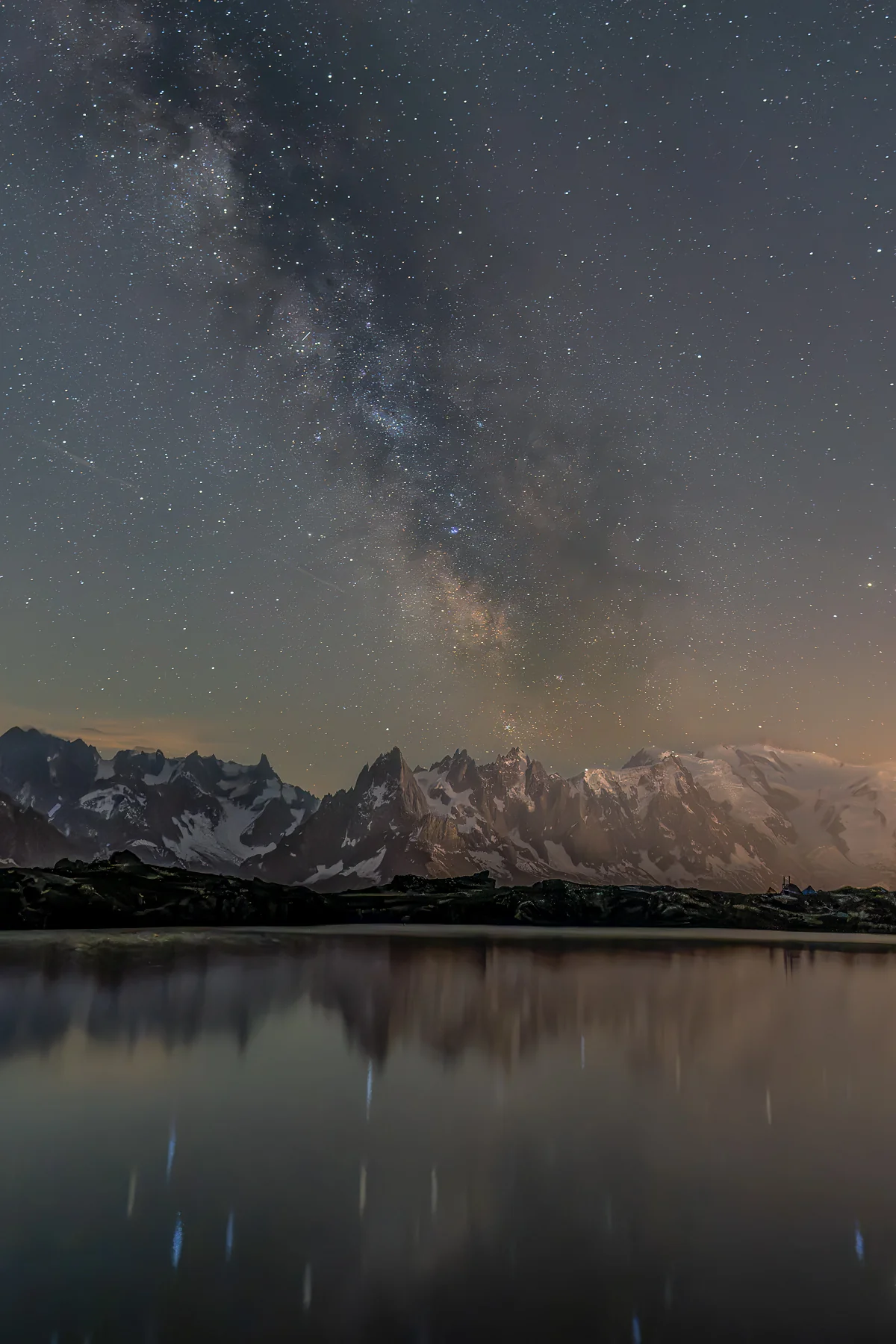 Spiegelnder Bergsee mit schneebedeckten Alpengipfeln und leuchtender Milchstraße am Nachthimmel