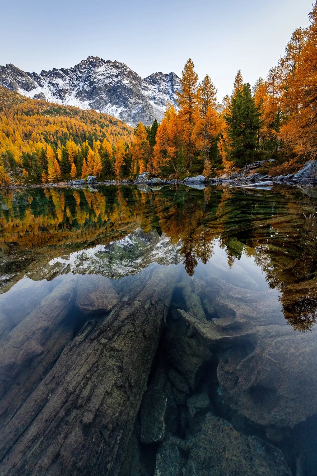 Spiegelnder Bergsee mit goldenen Lärchen und schneebedecktem Alpengipfel in Graubünden bei Herbstsonnenuntergang