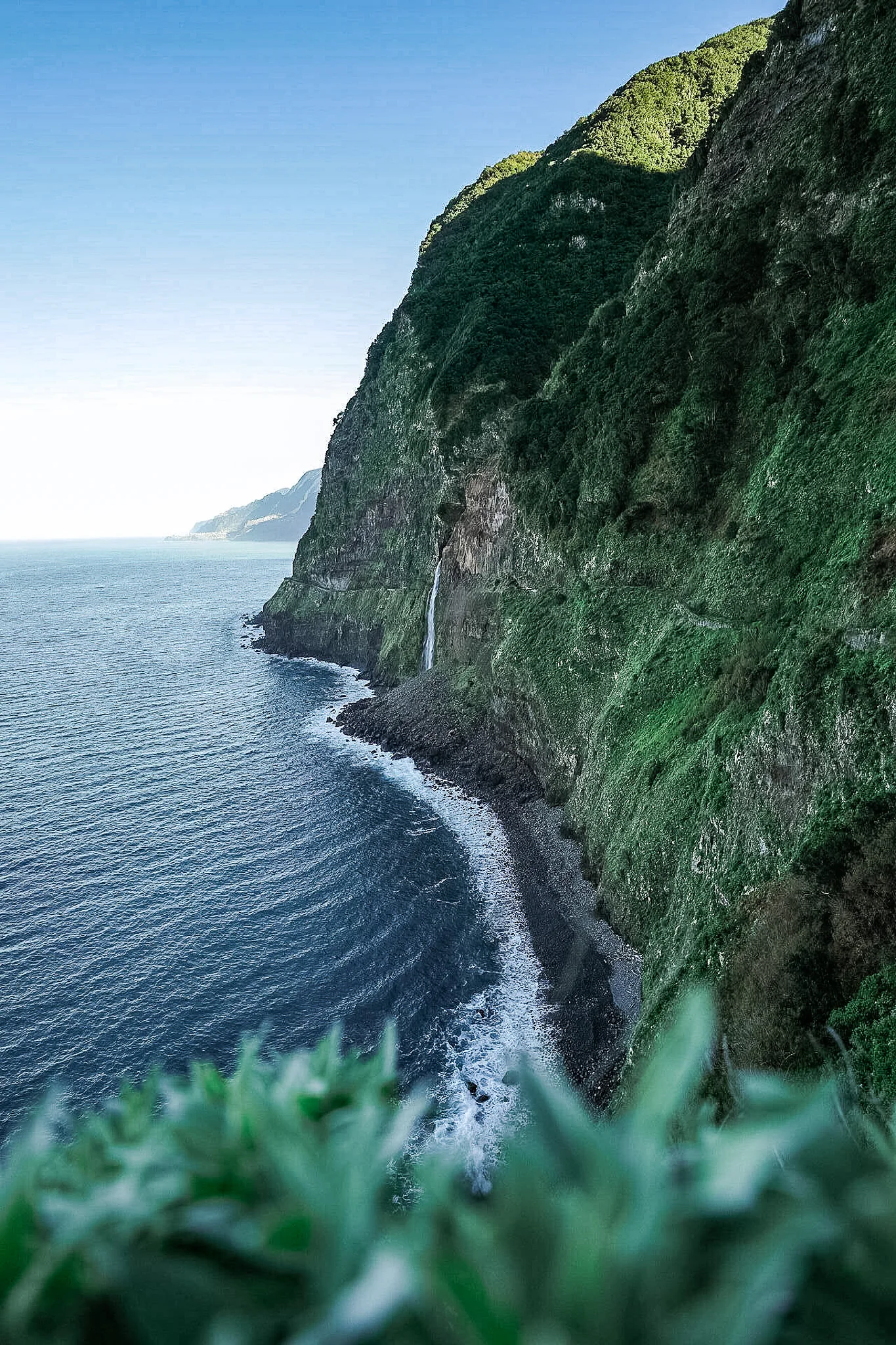Dramatische Steilküste von Madeira mit Wasserfall, dichter Vegetation und dem Atlantischen Ozean
