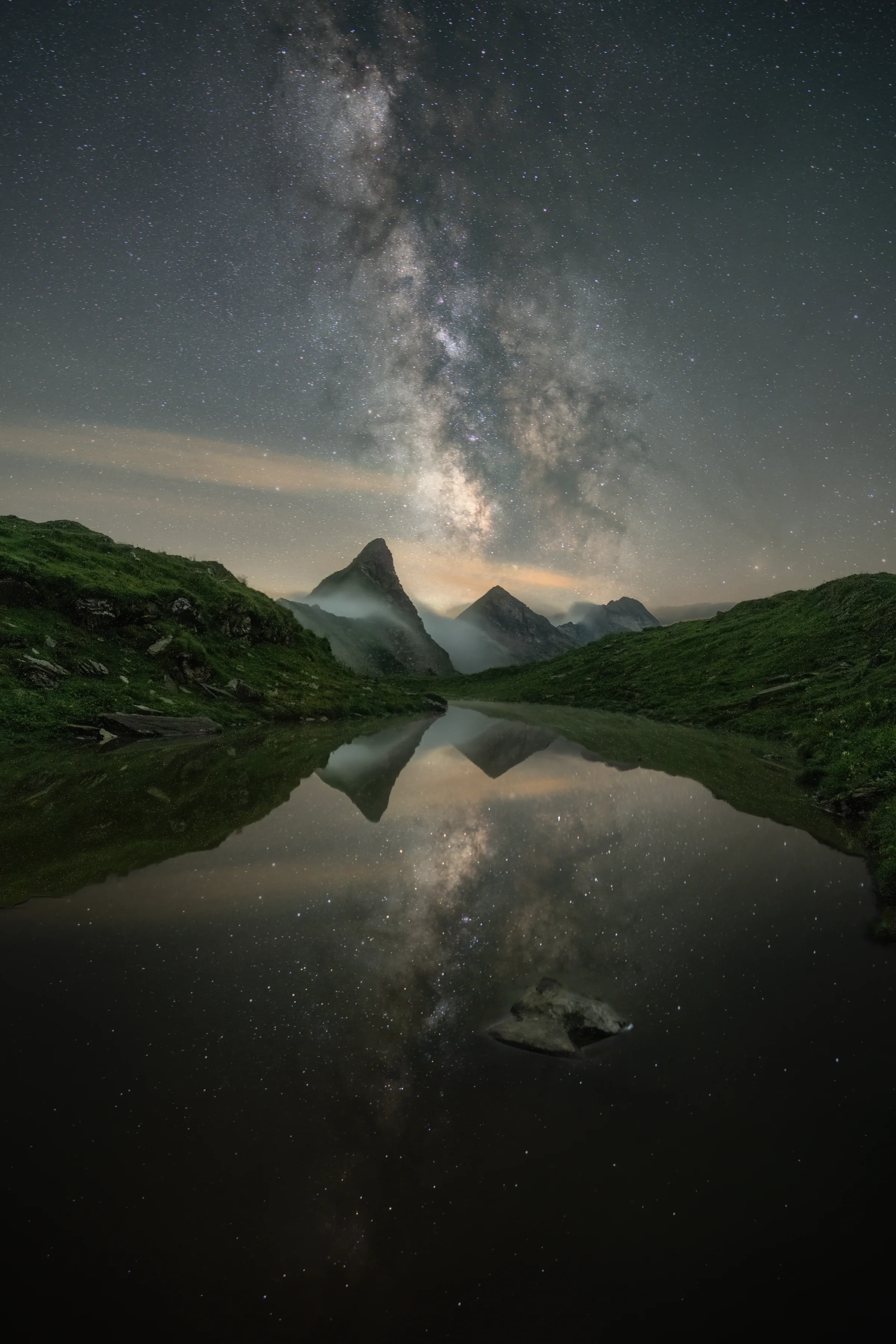 Majestätische Milchstraße spiegelt sich in einem ruhigen Bergsee, umgeben von grünen Alpengipfeln in der Nacht