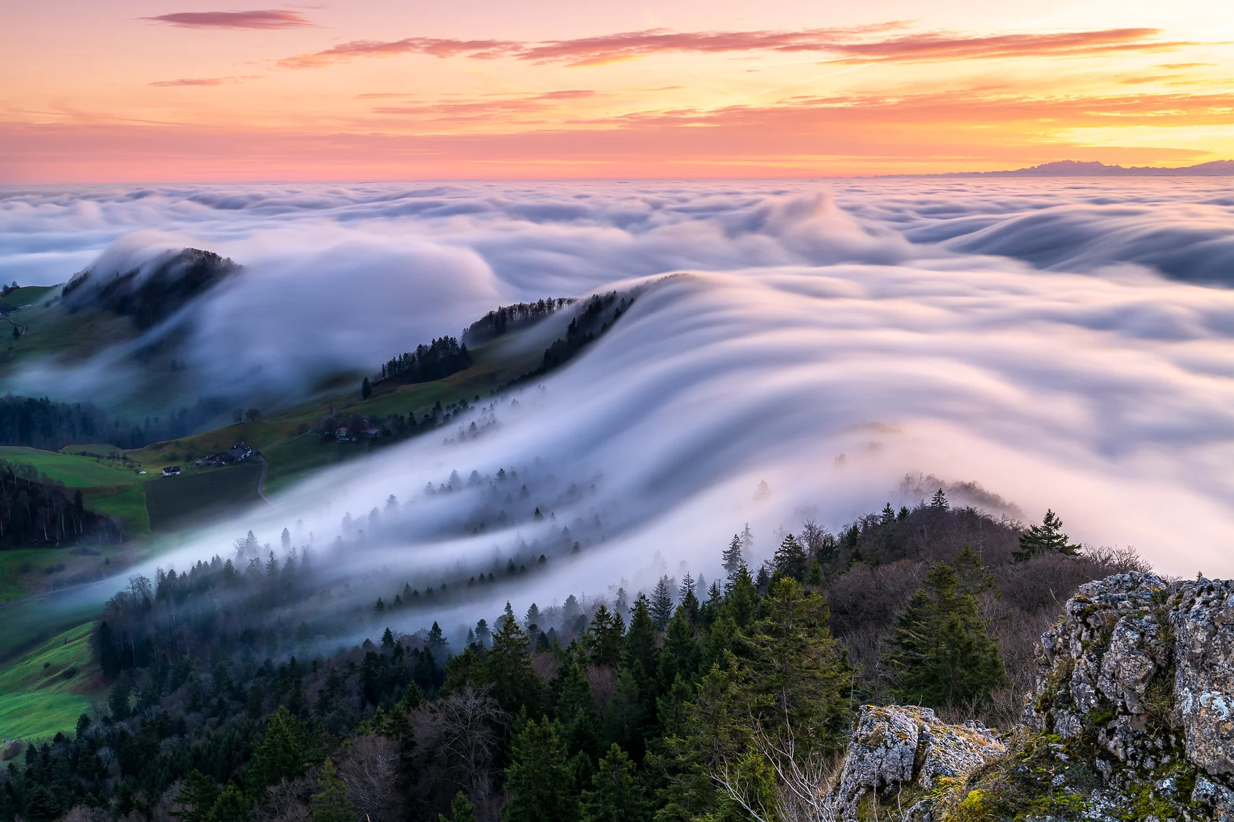 Dramatisches Nebelmeer mit Wolkenwellen bei Sonnenaufgang über bewaldeten Berghängen in Baselland