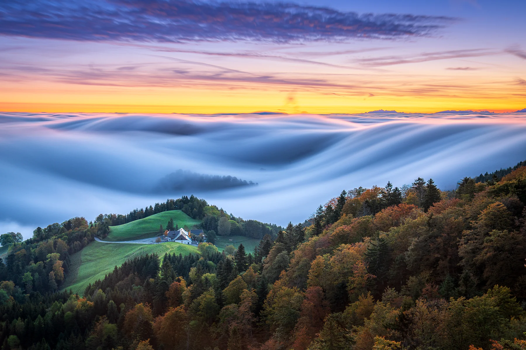 Magisches Nebelmeer mit Hügeln und Herbstwald bei goldenem Sonnenaufgang in Baselland