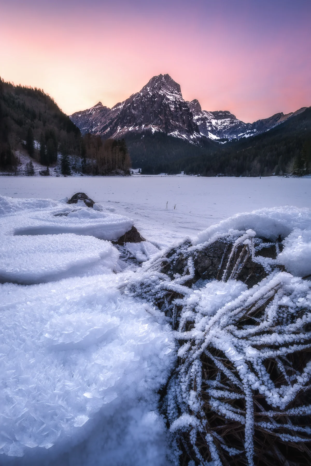 Gefrorener Obersee in Glarus mit schneebedecktem Bergpeak und Eiskristallen bei dramatischem Wintersonnenuntergang