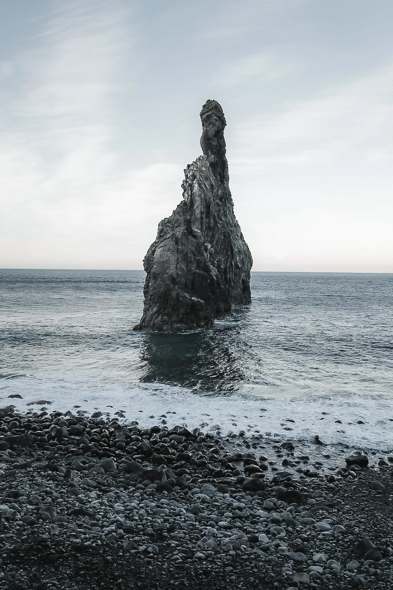 Imposante schwarze Felsnadel in der Ribeira da Janela, Madeira, umgeben von Atlantik und Kieselstrand