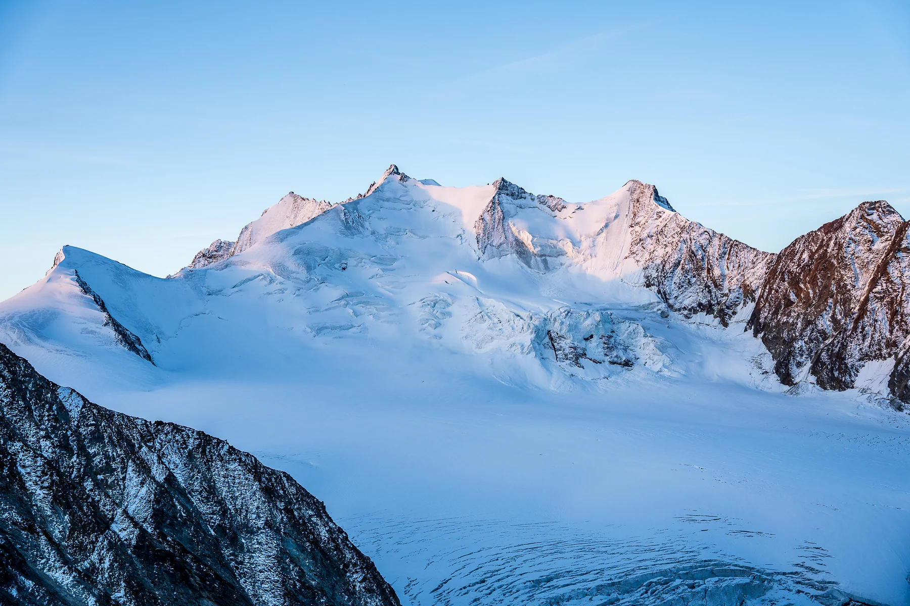 Schneebedeckter Riedgletscher mit rosa Alpengipfeln bei Sonnenaufgang in Wallis
