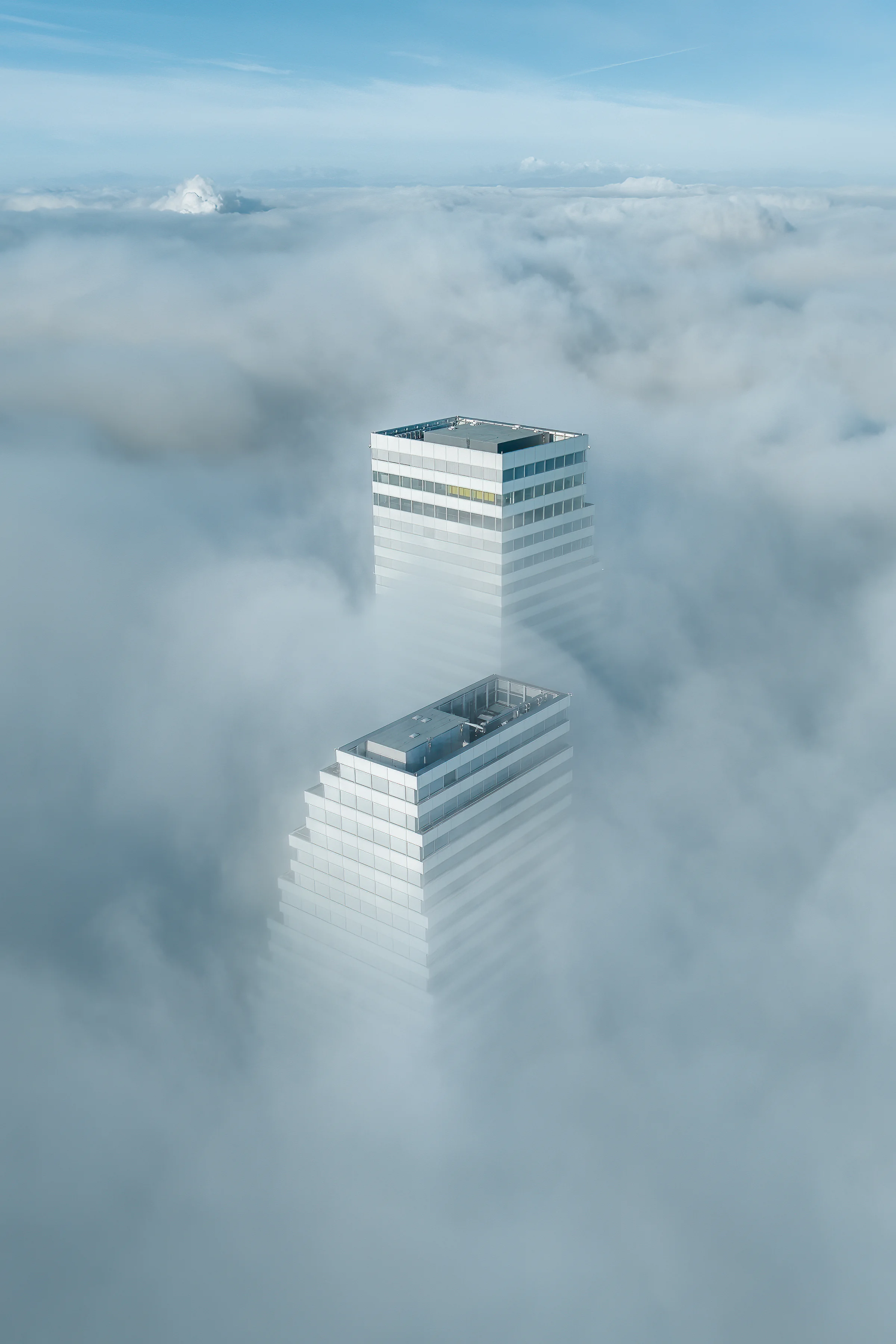Zwei moderne Hochhäuser der Roche Towers in Basel ragen aus einem dichten Nebelmeer heraus, fotografiert von einer Drohne