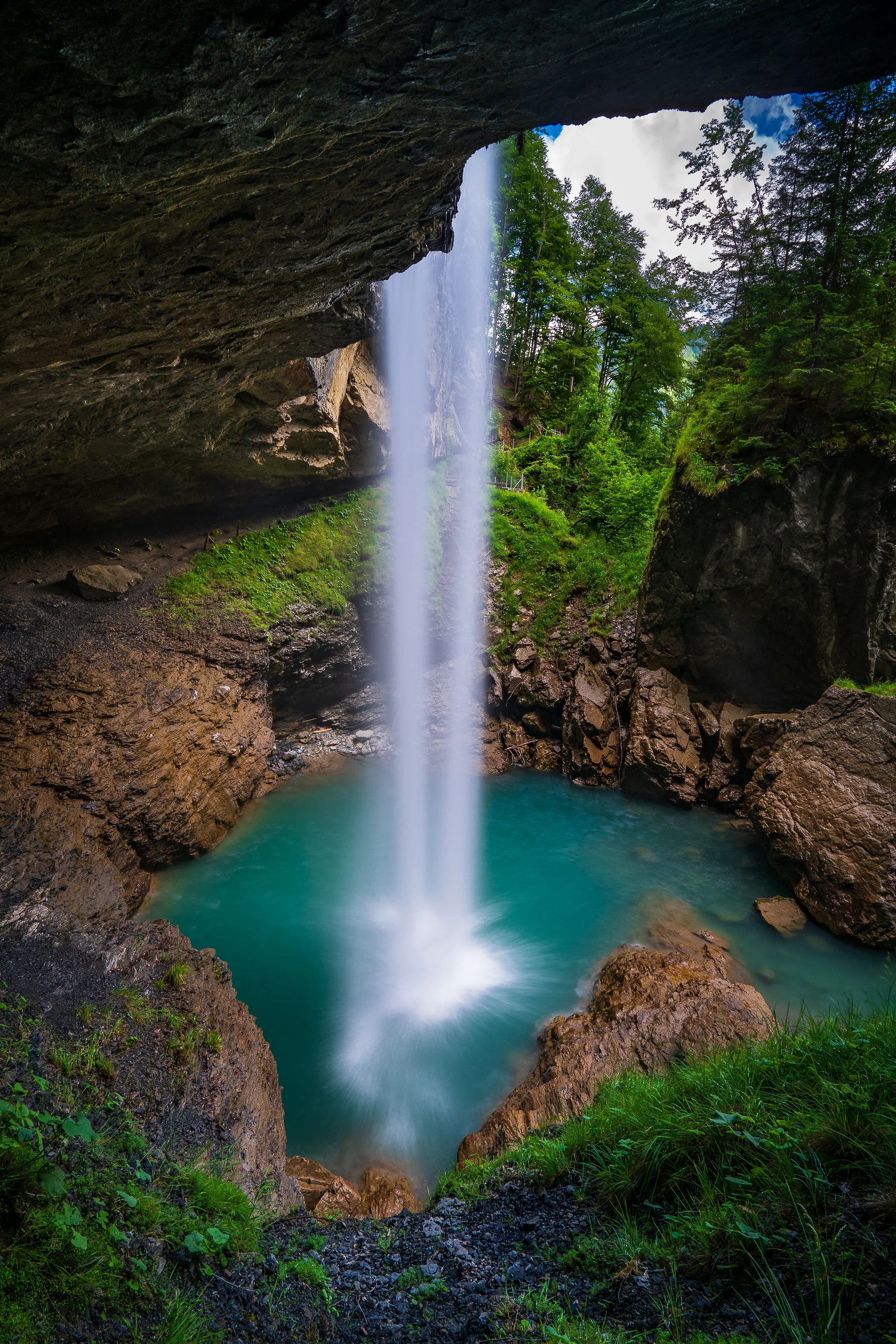 Majestätischer Wasserfall mit türkisem Naturbecken in einer Felskluft, umgeben von üppiger Vegetation in Glarus